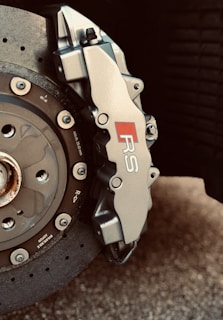 Close-up view of a high-performance vehicle brake system featuring a ventilated disc and a caliper with an RS logo. The disc is metallic with visible bolts, while the caliper appears sleek and robust.