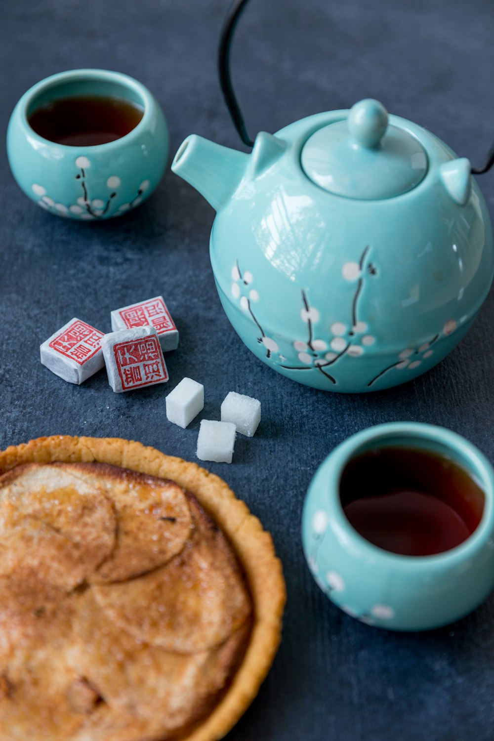 blue and white ceramic teapot beside brown bread on brown wooden table