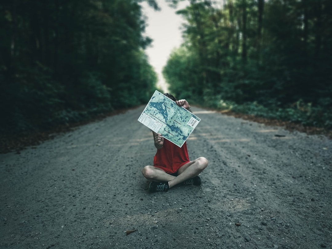 woman in pink dress holding umbrella sitting on gray concrete road during daytime