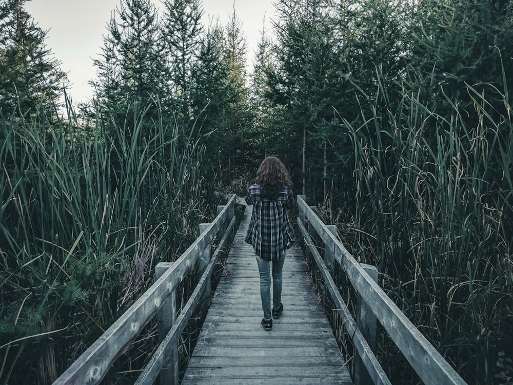 woman walking on wooden bridge between green grass during daytime