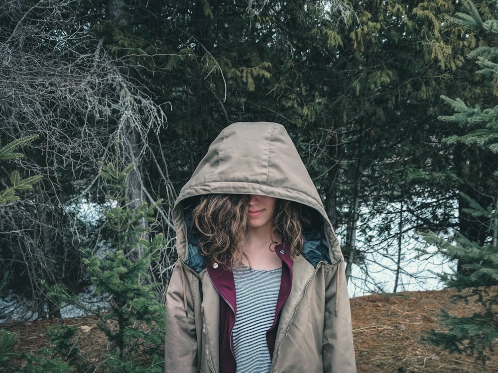 woman in brown coat standing near green trees during daytime