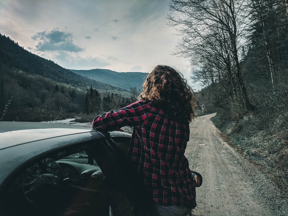 woman in black and red plaid dress shirt standing beside black car during daytime