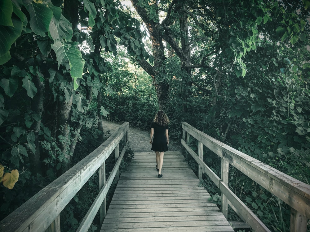 woman in black dress walking on wooden bridge