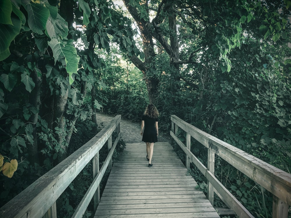 femme en robe noire marchant sur un pont en bois