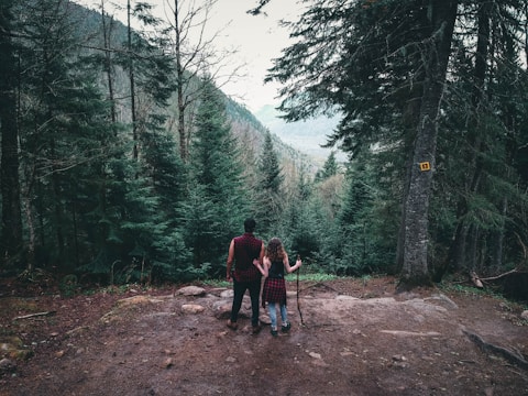 2 men walking on dirt road between trees during daytime