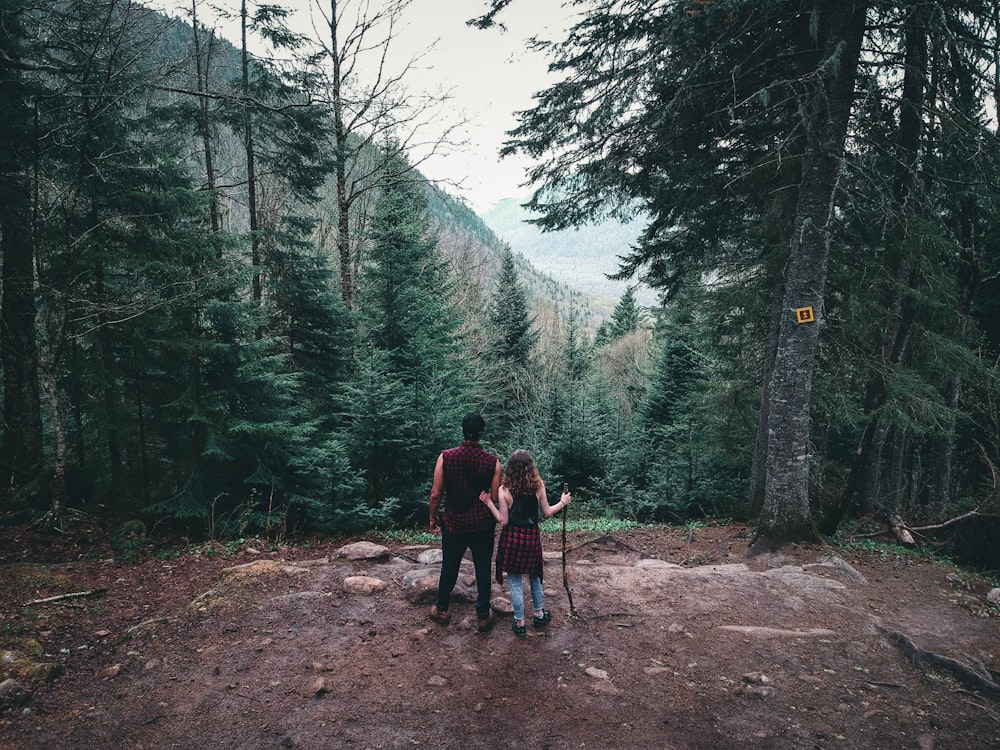 2 men walking on dirt road between trees during daytime