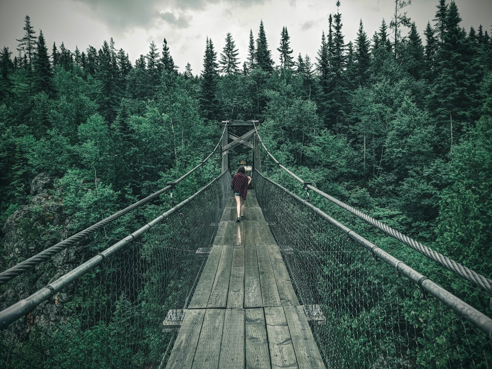 Persona con chaqueta negra caminando en puente colgante