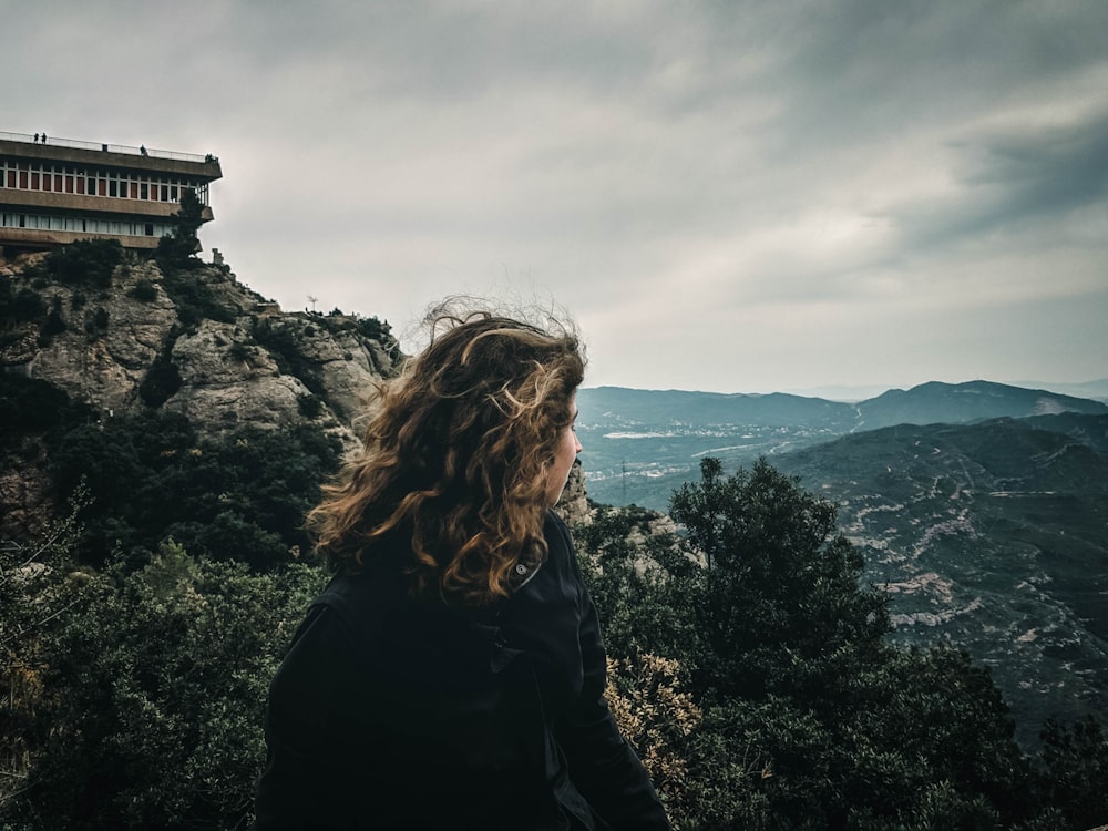 Mujer con chaqueta negra de pie en la cima de la montaña durante el día