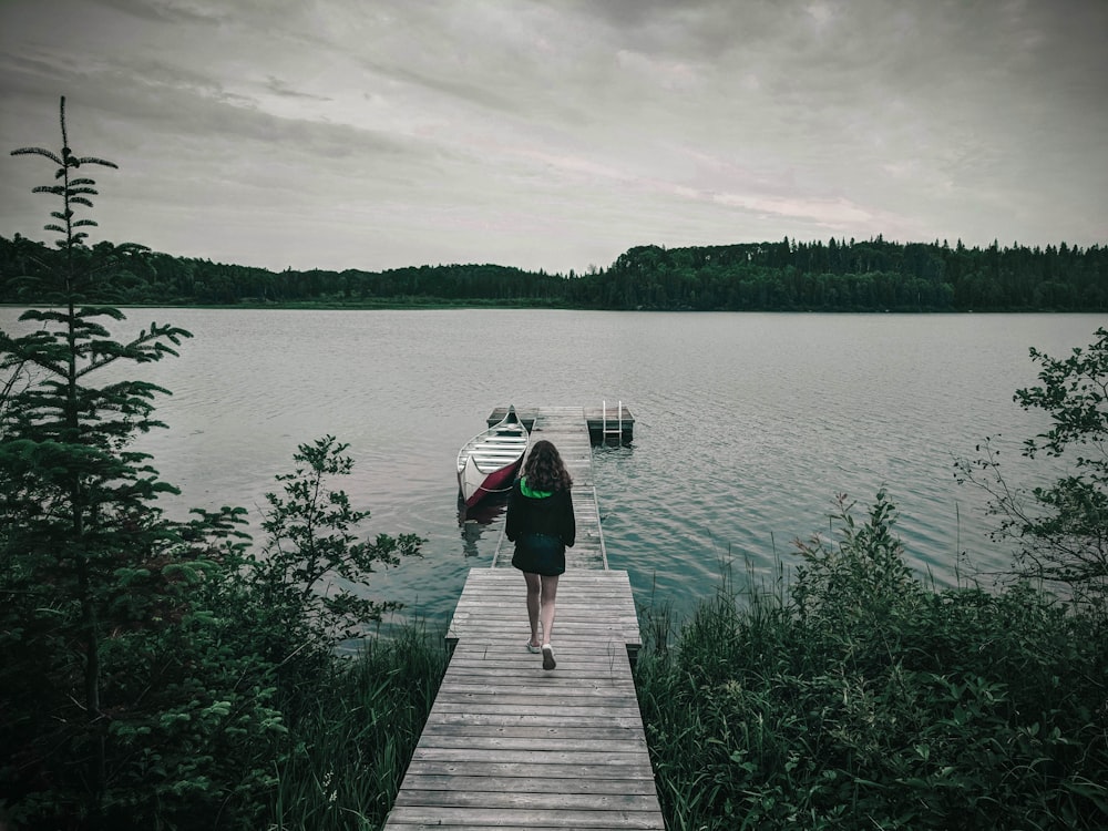 person in black jacket and blue denim jeans walking on wooden dock during daytime