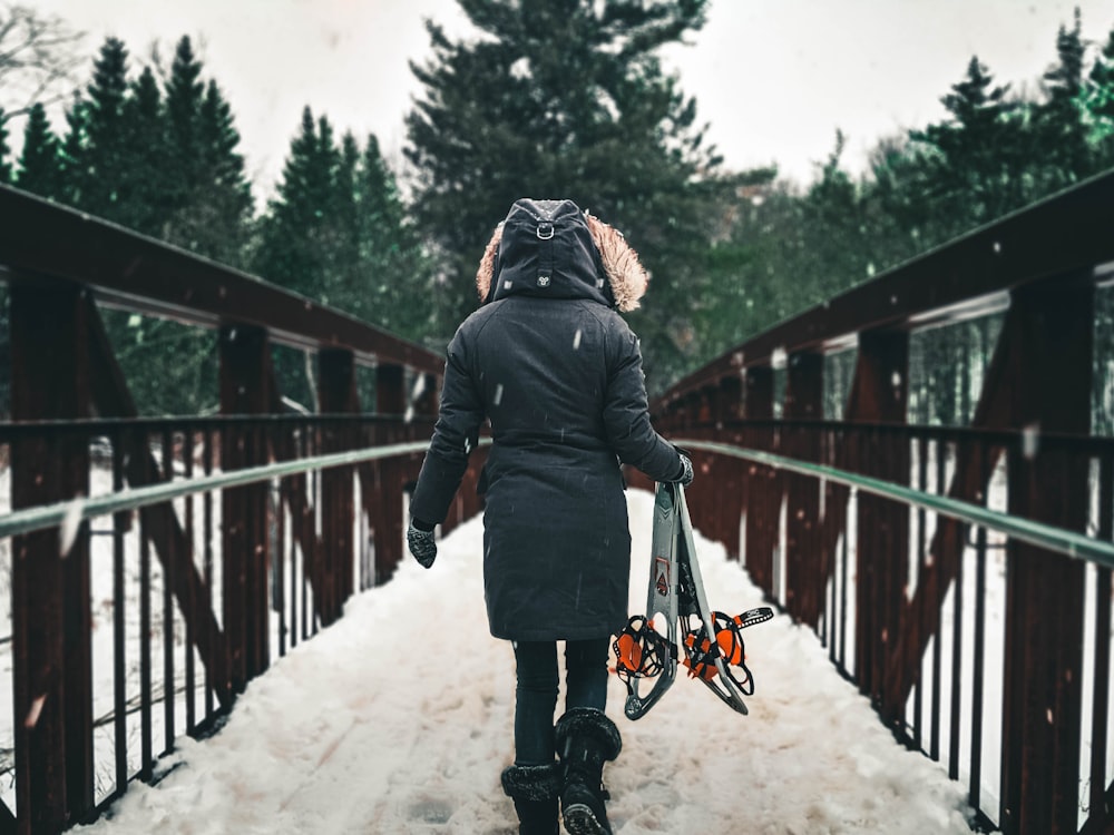 person in black jacket and black pants walking on snow covered bridge during daytime