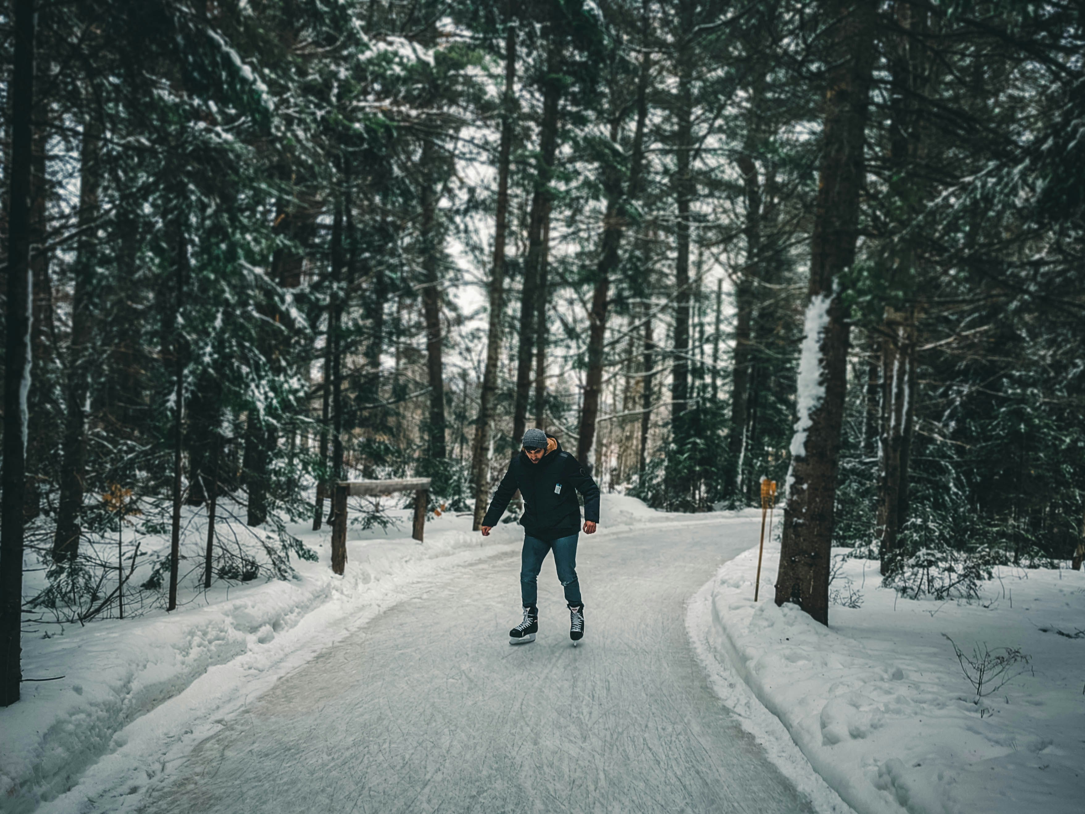 person in black jacket and black pants walking on snow covered pathway between trees during daytime