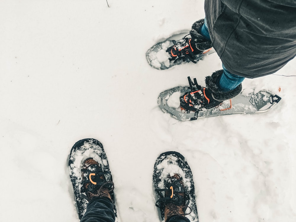 黒いズボンと黒と白のスノースキーシューズを履いた人が雪に覆われた地面に立っています