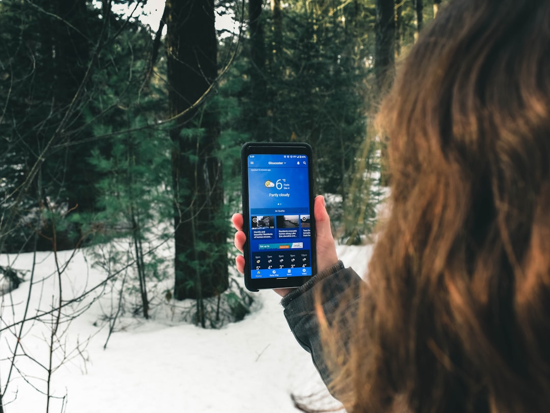 woman holding black smartphone taking photo of trees during daytime