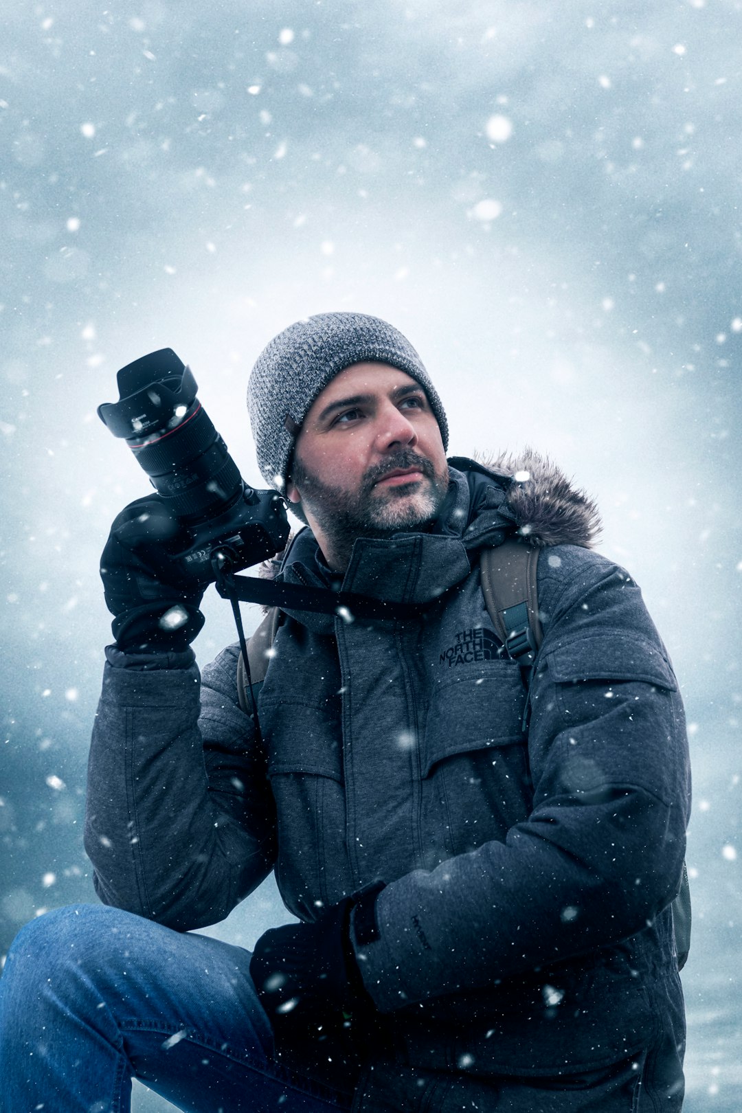 man in black jacket and knit cap holding black dslr camera