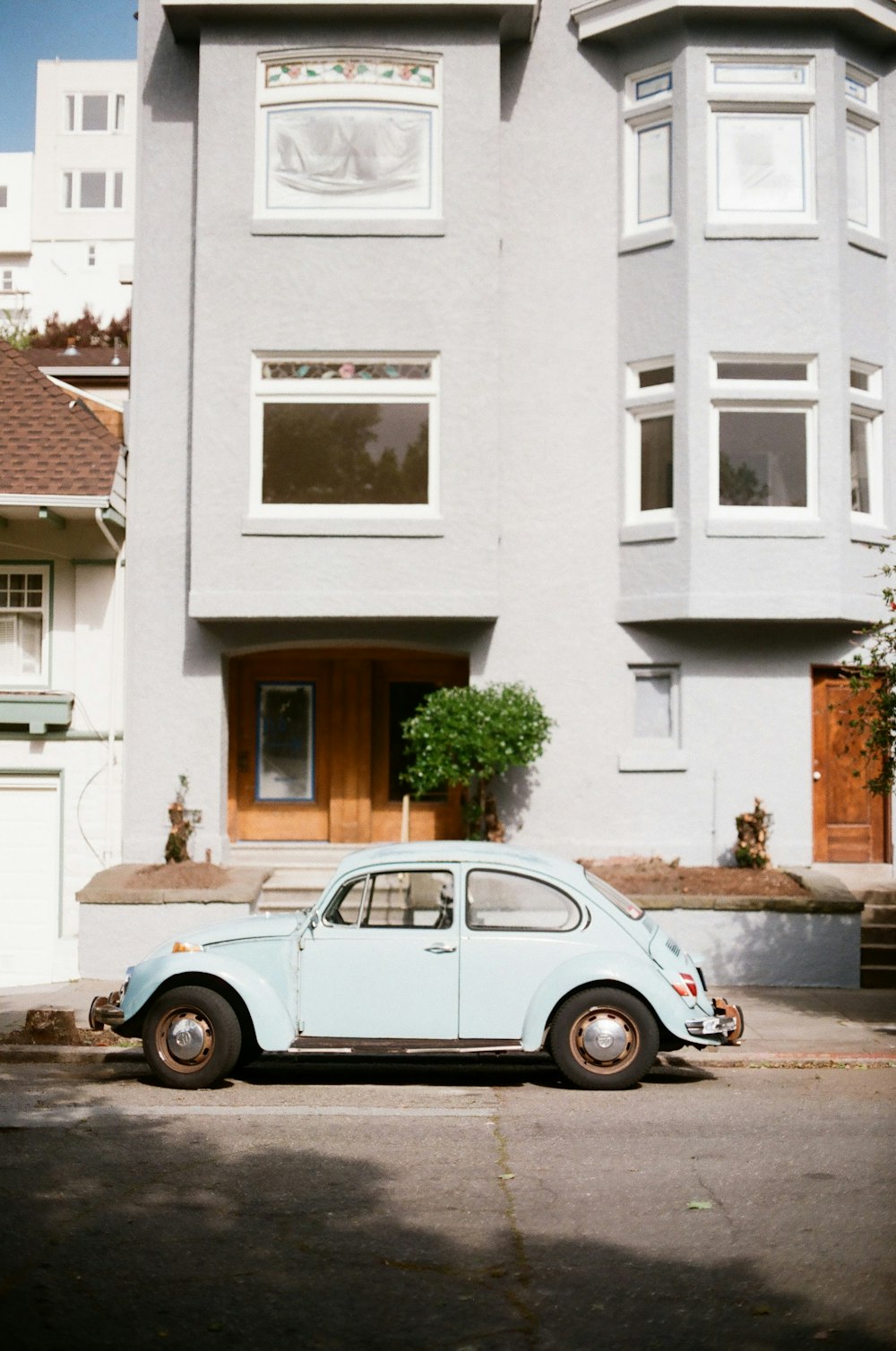 blue volkswagen beetle parked beside white concrete building during daytime