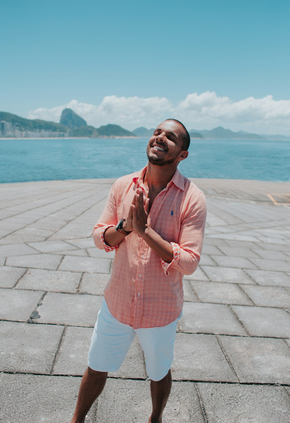 uomo in camicia rosa in piedi sul marciapiede di cemento grigio vicino allo specchio d'acqua durante il giorno