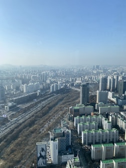 A sprawling cityscape with numerous tall buildings, apartment complexes, and transportation infrastructure. The image includes high-rise structures with green roofs and a large mural on a building in the foreground. The image stretches into the horizon, displaying a vast expanse of urban development.