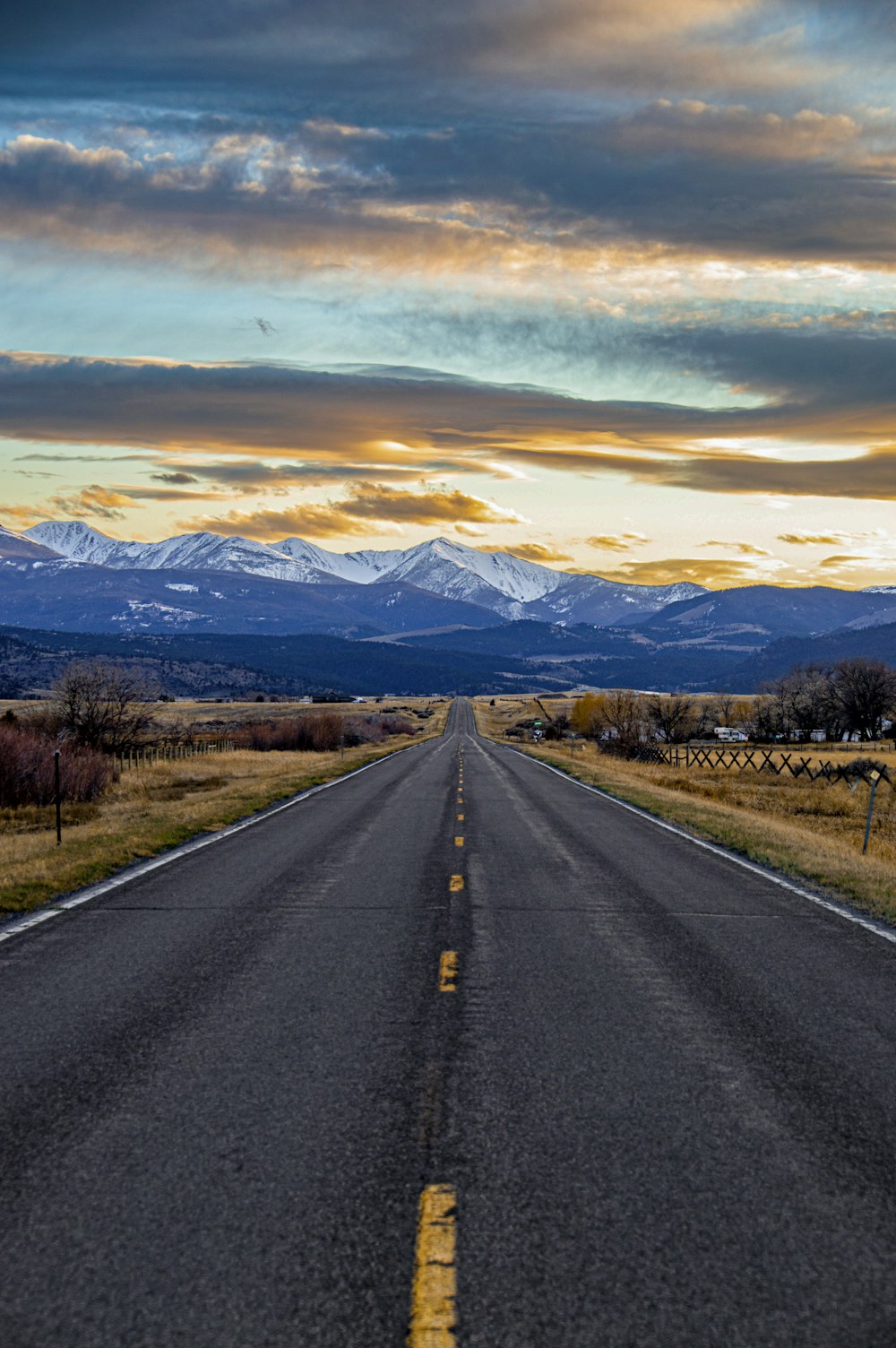 gray asphalt road between green grass field under blue sky during daytime