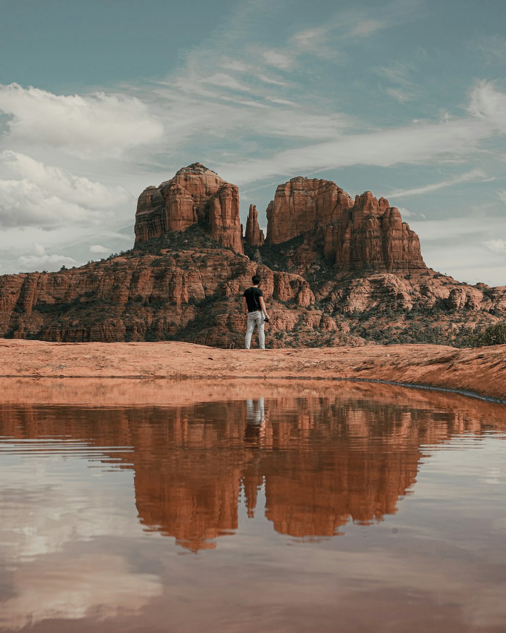 person in white shirt walking on brown sand near brown rocky mountain under white clouds during