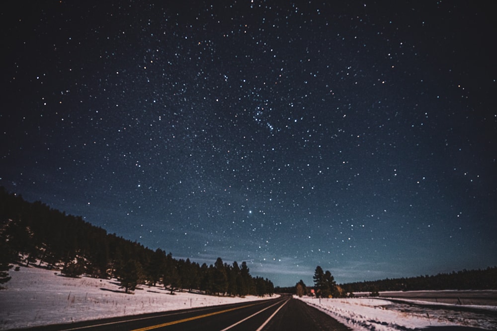 black asphalt road between snow covered ground under starry night