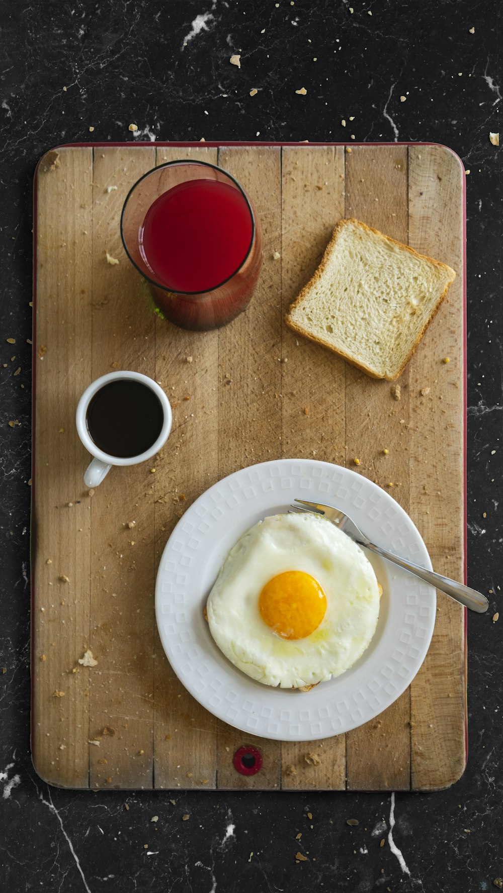 透明なコップに入った赤い液体の横の白いセラミックの丸い皿に卵