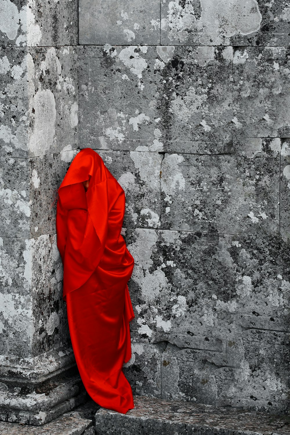person in red robe standing on gray concrete wall