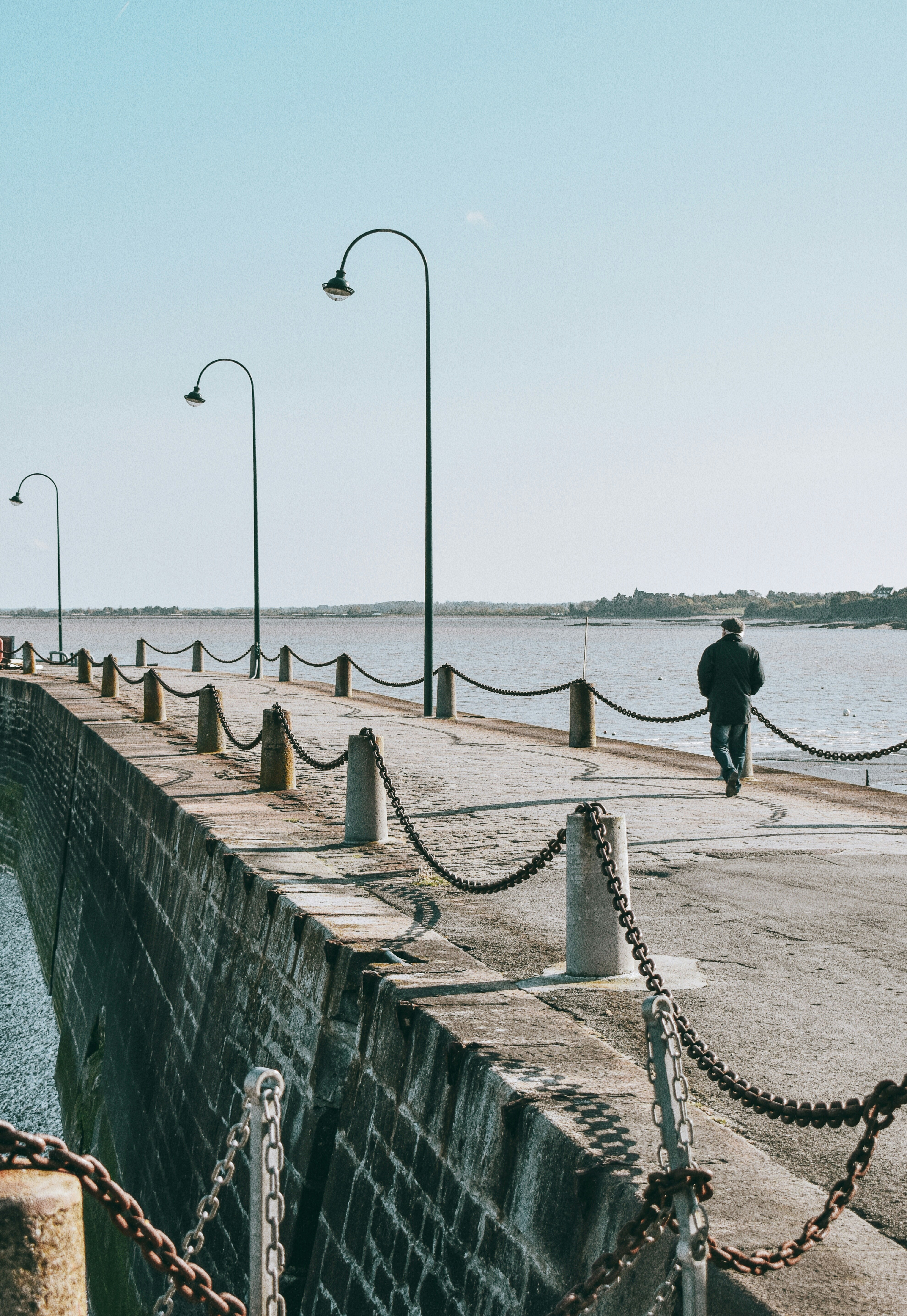 man in black jacket and black pants walking on brown wooden dock during daytime