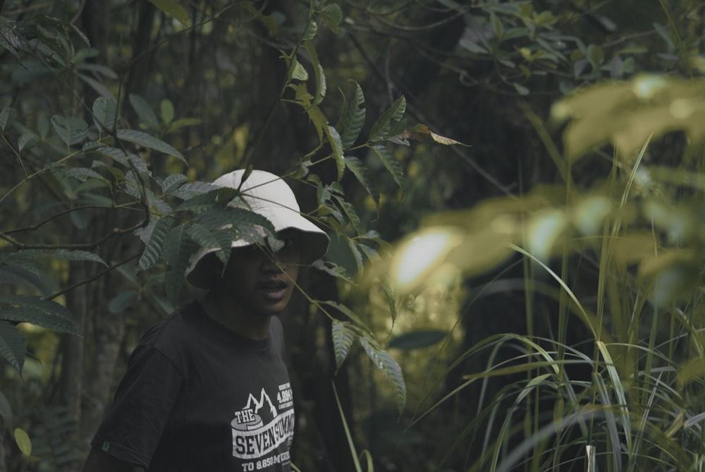 homme en sweat à capuche noir portant un chapeau blanc debout près de plantes vertes pendant la journée