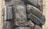A towering stack of old, weathered suitcases and bags, arranged haphazardly and exposed to the elements. The suitcases, mostly vintage in style, exhibit signs of wear and age, with faded and peeling surfaces. The setting appears to be outdoors, likely in an urban area.