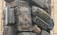 A towering stack of old, weathered suitcases and bags, arranged haphazardly and exposed to the elements. The suitcases, mostly vintage in style, exhibit signs of wear and age, with faded and peeling surfaces. The setting appears to be outdoors, likely in an urban area.