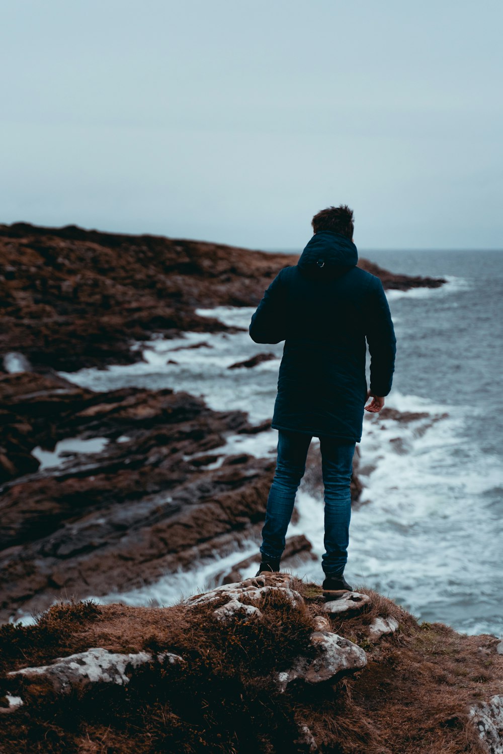 man in black jacket standing on rock formation near sea during daytime