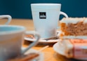 white ceramic mug on white ceramic saucer beside bread on white ceramic plate