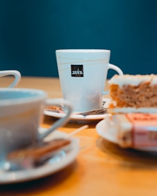 white ceramic mug on white ceramic saucer beside bread on white ceramic plate