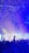 A vibrant concert scene with a multitude of confetti raining down over an enthusiastic crowd. Silhouetted hands are raised in celebration, while colorful lights illuminate the stage, creating a lively and festive atmosphere.