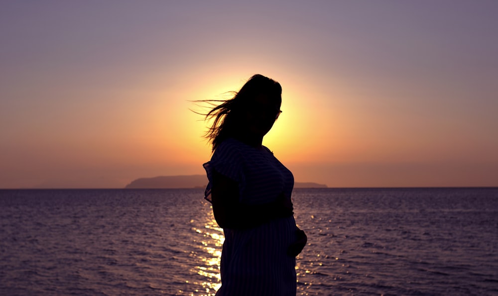 silhouette of woman standing on beach during sunset