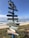 A colorful signpost stands on a beach, with several directional arrows pointing to various international locations. The sea and sky form a serene backdrop, with gentle waves rolling onto the shore.