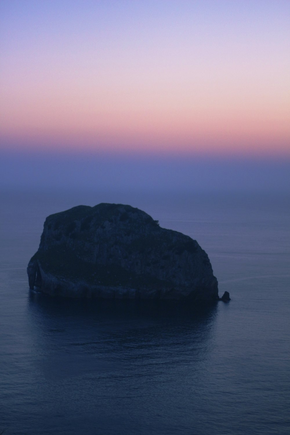 black rock formation on body of water during sunset