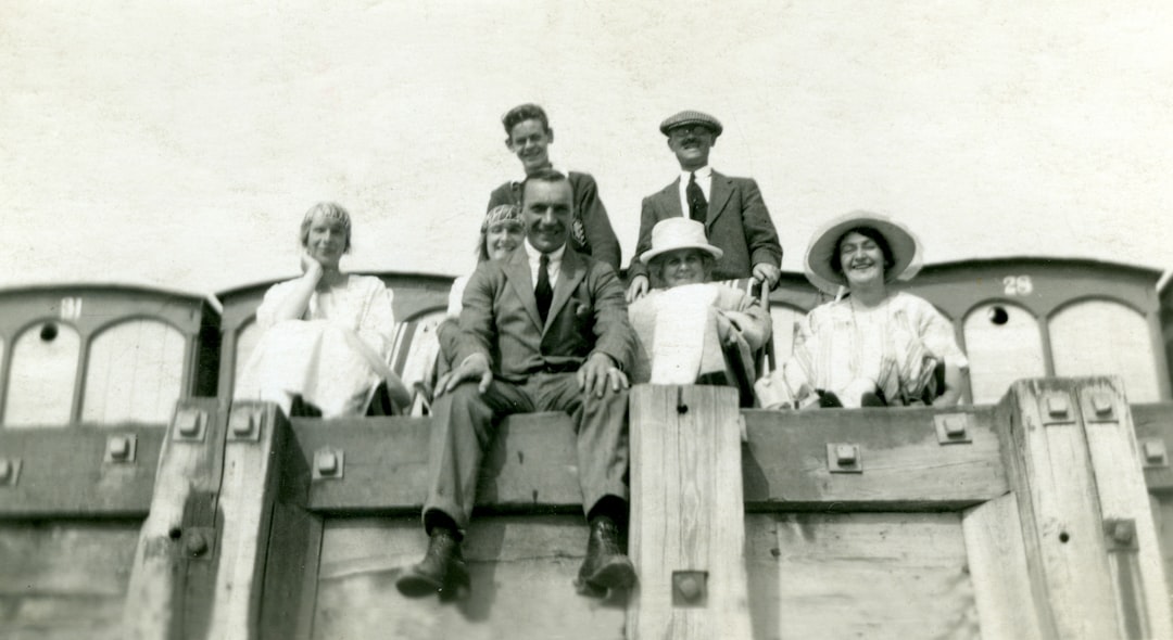 grayscale photo of 3 men and 2 women sitting on wooden bench