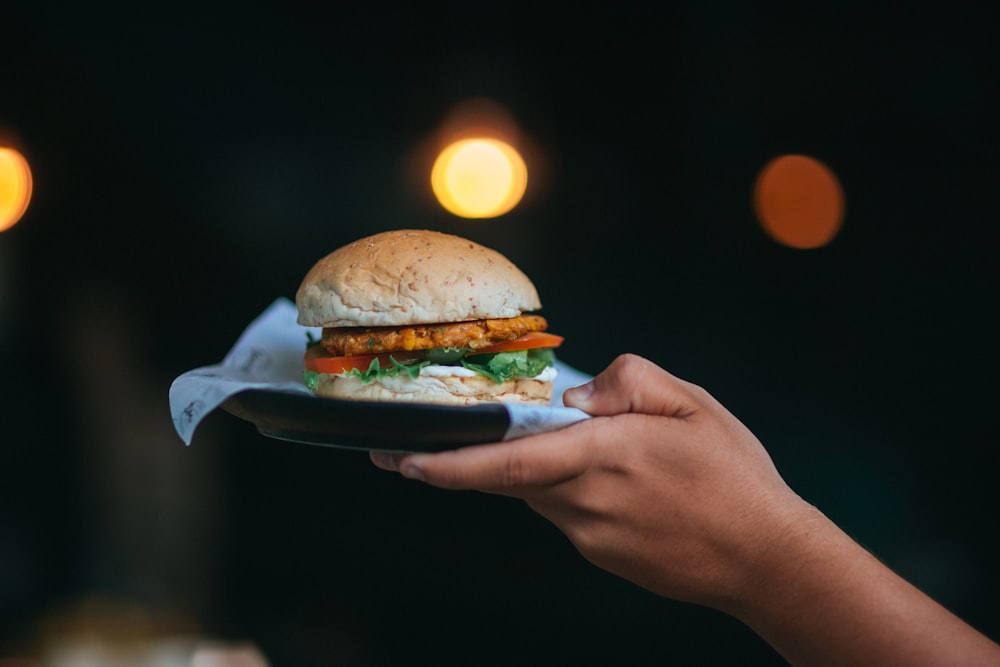 person holding burger with lettuce and tomato