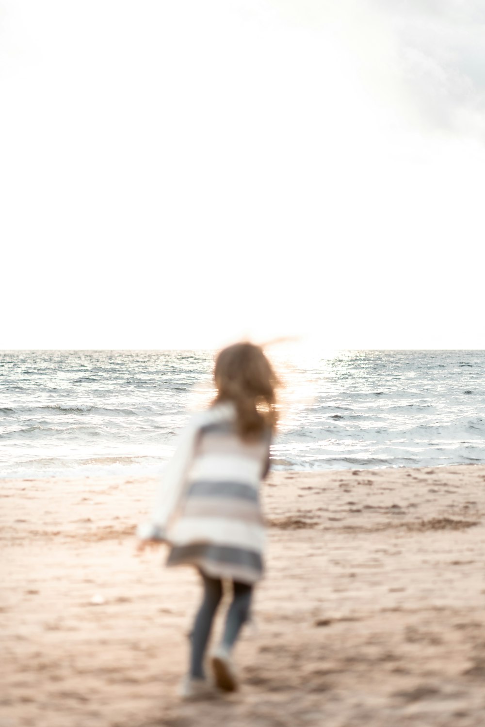 Femme en chemise à manches longues à rayures blanches et bleues debout sur la plage pendant la journée