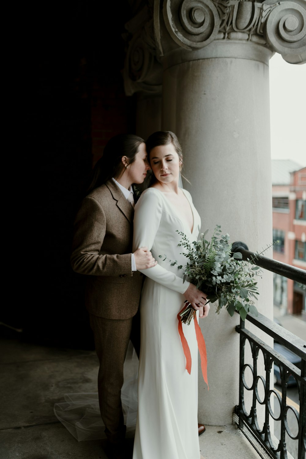 man in brown suit and woman in white wedding dress standing beside brown concrete wall during