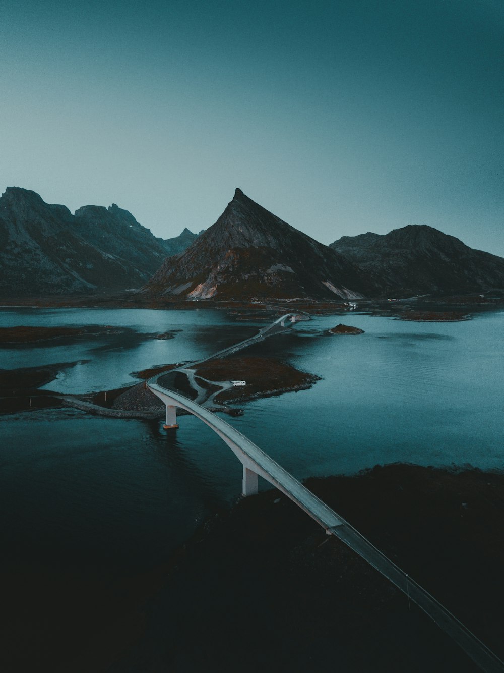 昼間の湖と山に架かる白い橋