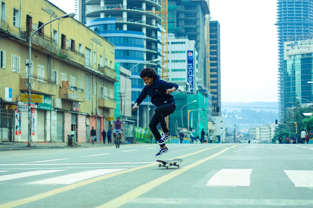 검은 셔츠와 검은 바지를 입은 남자가 낮 동안 회색 콘크리트 도로에서 스케이트보드 스턴트를 하고 있다