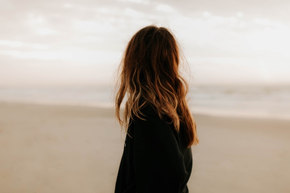 昼間のビーチに立つ黒いジャケットの女性