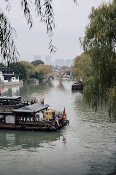 A serene riverside scene in Dali, with traditional Chinese boats and misty mountains in the background.