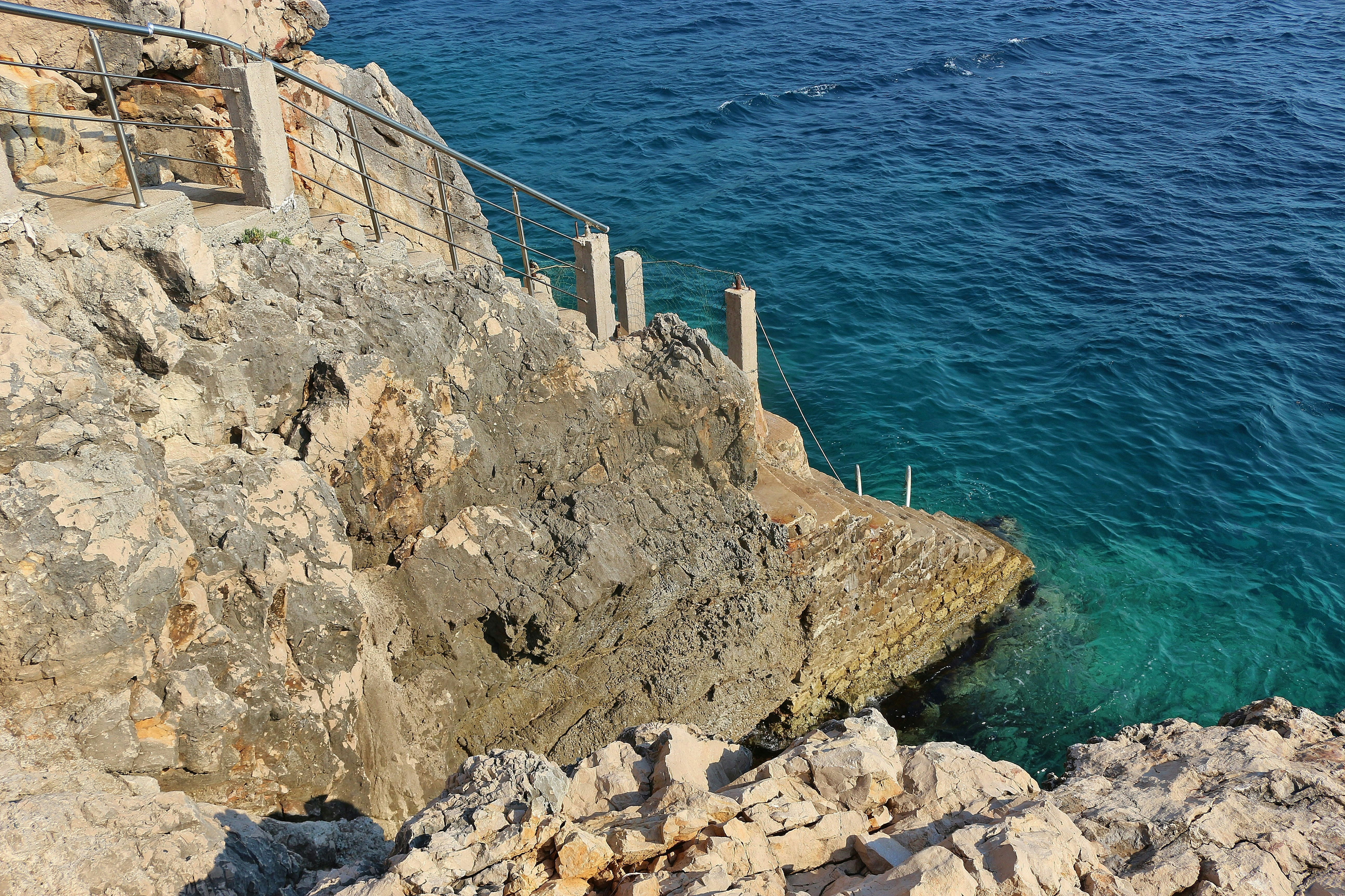 brown rock formation near body of water during daytime, Steep stairs leading down the cliffs to the very blue adriatic sea. Dobra Voda, Montenegro, Southeast Europe.
