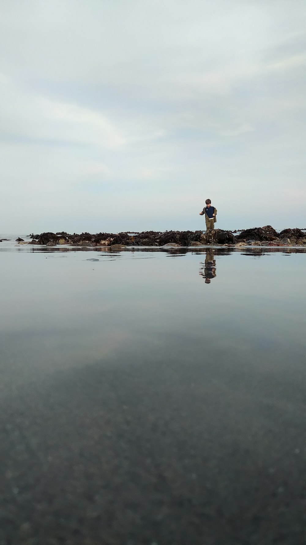 man in black shirt standing on brown rock formation in the middle of water during daytime