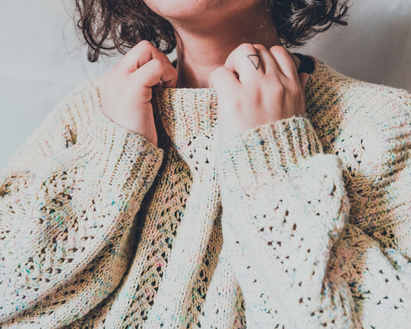 Close-up of a cream open-knit cardigan held at the collar