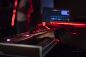 Musician playing keyboard with headphones in a studio illuminated by red and black ambient lights
