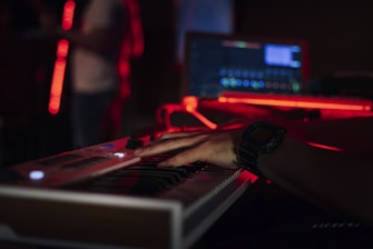 Musician playing keyboard with headphones in a studio illuminated by red and black ambient lights